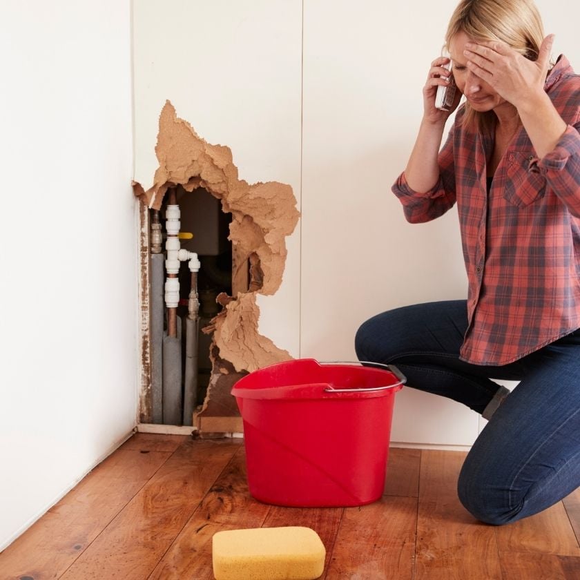 woman on floor by burst pipe in wall