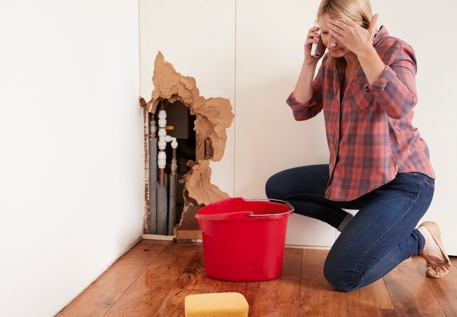 woman on floor by burst pipe in wall