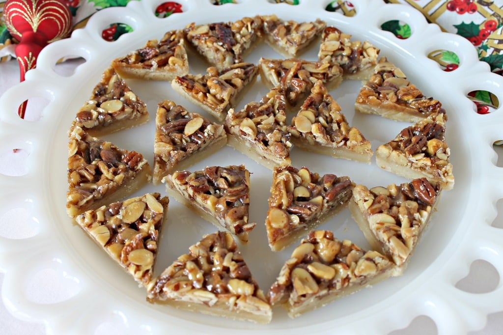 Triple Nut Bar Cookies recipe. Bar cookies are a must for Christmas. These triple nut bar cookies are pretty and delicious too! #Christmascookies #barcookies nut topped bar cookies sliced into triangles and served on a white platter