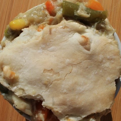 Chicken pot pie with vegetables spilling out of the top crust in a white bowl