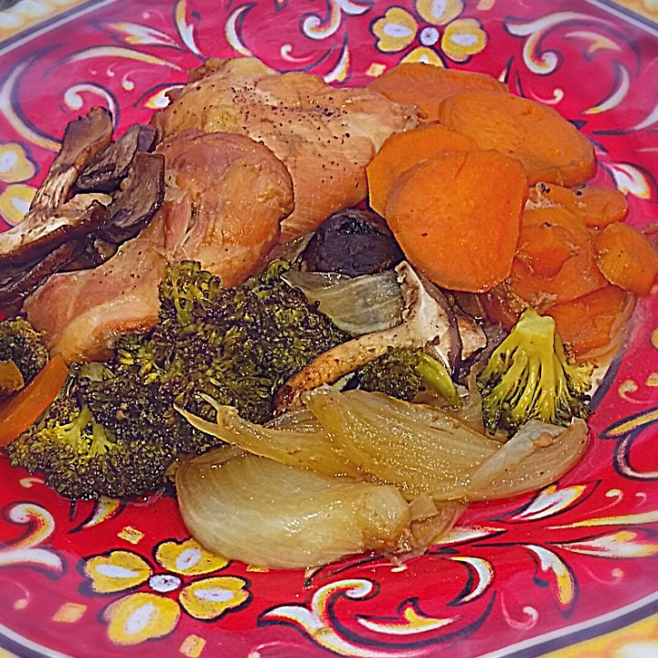 Boneless skinless chicken thighs cooked and ready to eat on a colorful plate next to cooked vegetables