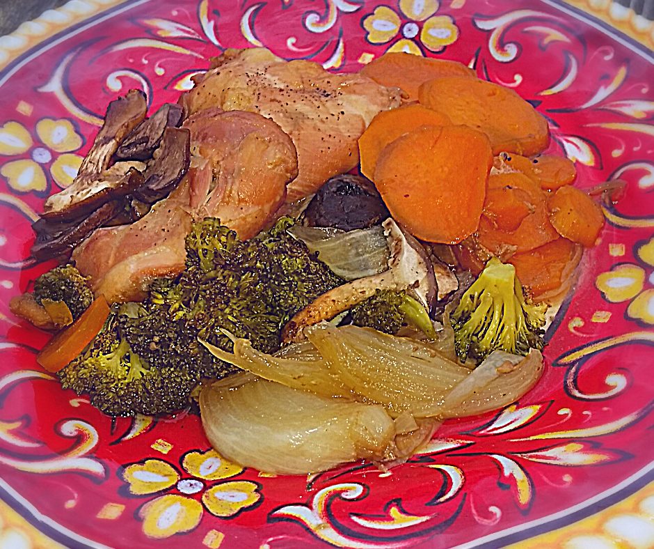 Boneless skinless chicken thighs cooked and ready to eat on a colorful plate next to cooked vegetables