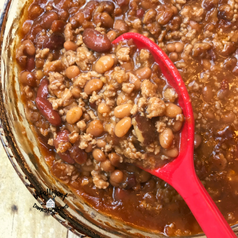 Baked beans in a big bowl with a red spoon lifting some up