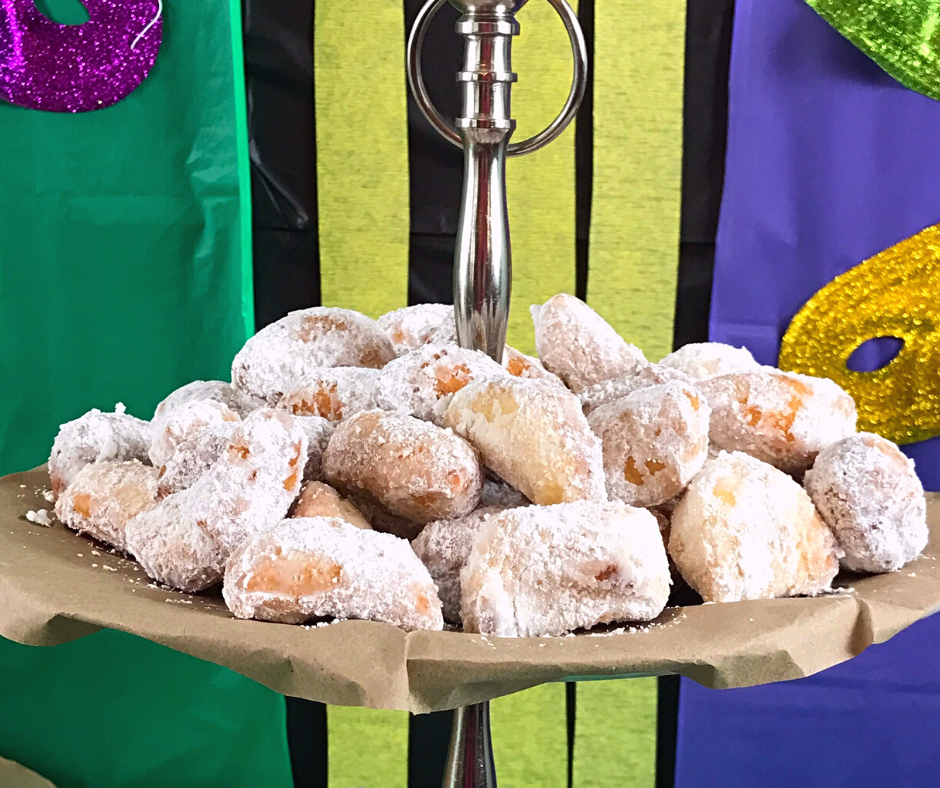 Biscuit Biegnets served on a tiered tray with green, gold and purple decorations including Mardi Gras masks