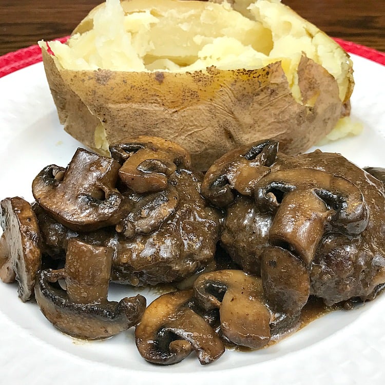 Homemade Chopped Steak and mushroom gravy served with a Baked Potato Chopped steak with gravy and mushrooms next to a baked potato on a white plate