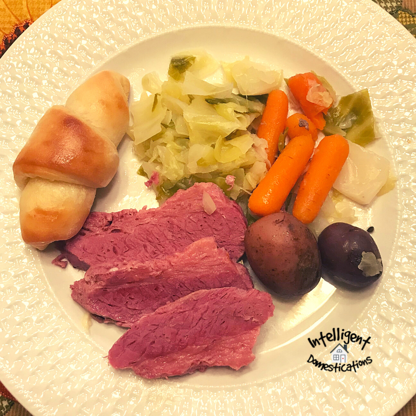 A dinner plate with Corned Beef, Cabbage, Carrots and Potatoes with a roll
