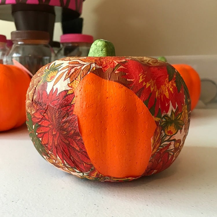 Use a pretty Fall Napkin to create this Dollar Store Pumpkin Makeover. It is a decoupage project and cheap decor project. Fall Napkin being glued onto a Dollar Store Pumpkin with just one spot left to cover