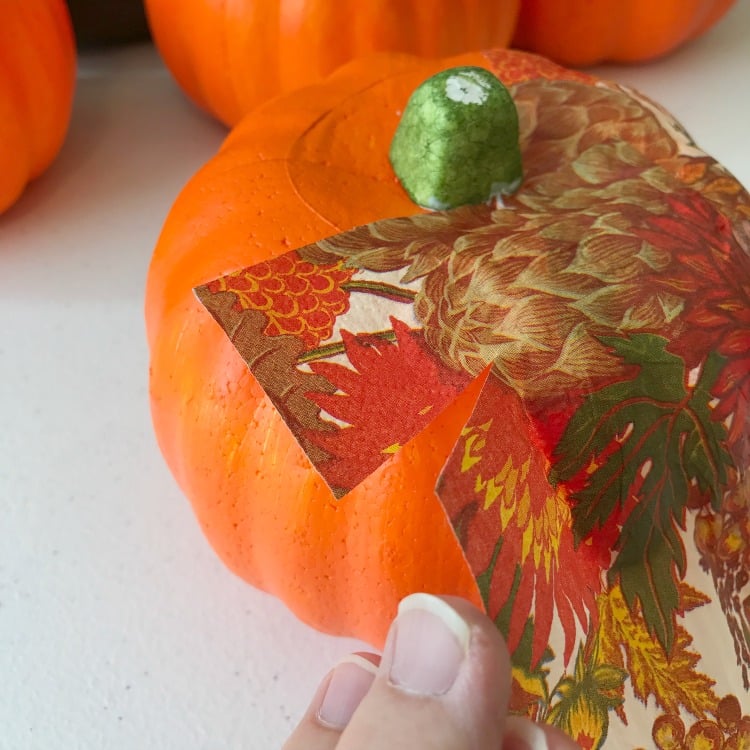 Use a pretty Fall Napkin to create this Dollar Store Pumpkin Makeover. It is a decoupage project and cheap decor project. Fall Napkin being glued onto a Dollar Store Pumpkin