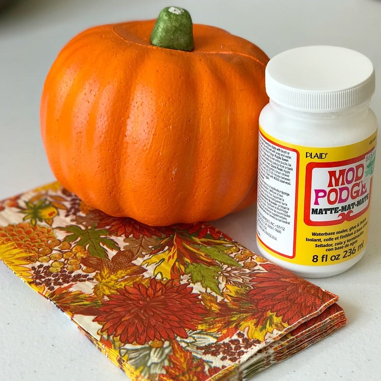 Fall napkins, a dollar store orange pumpkin and Mod Podge decoupage glue all on a white background