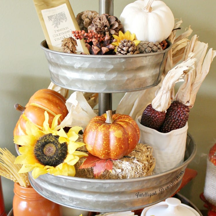 Top two tiers of a galvanized three tier tray decorated for fall with pumpkins, flowers, pine cones and dried corn