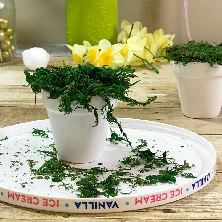 Use hot glue to affix the faux grass moss onto the pot
