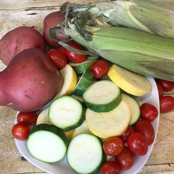 Fresh vegetables used in making a foil pack dinner. Foil pack dinner recipe. Zucchini, squash, cherry tomatoes, fresh corn and drumsticks make this foil pack dinner delightful and delicious. #foilpackdinner #hobodinner #foilpacketmeal