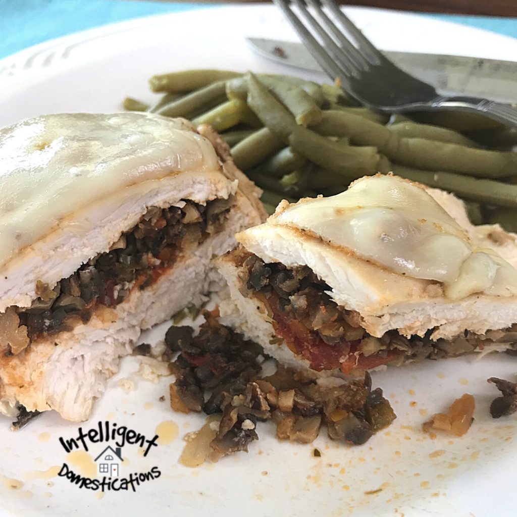 Stuffed Chicken Breast with cheese melted on top sliced in half on a white plate