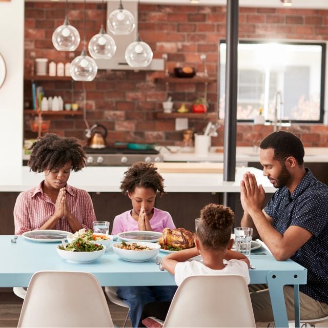 a family sitting at a table in front of their food saying their mealtime prayer