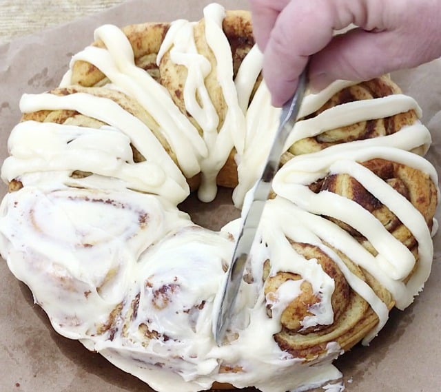 Cinnamon roll cake with icing piped on and the icing is being spread with a knife