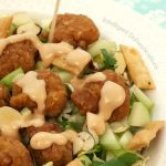 Salad in a white bowl with chicken tenders and dressing being poured over it