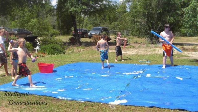 This one DIY Water Tarp Game will keep the kids busy with backyard summer water activities for hours! It's versatile for playing in the water. Play Water Balloon games, Water Bomb Target competitions. Pool Noodle Sword Fighting and a Slip and Slide surface and even use the Target Backdrop as a Photo spot! #watergames #summergames #outdoorplay This one DIY Water Tarp Game will keep the kids busy with backyard summer water activities for hours! It's versatile for playing in the water. Play Water Balloon games, Water Bomb Target competitions. Pool Noodle Sword Fighting and a Slip and Slide surface and even use the Target Backdrop as a Photo spot! #watergames #summergames #outdoorplay