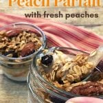 Two Mini Mason jars filled with a peach parfait recipe topped with granola displayed on a table with a red and white towel and one is being held in a hand with a spoon in the jar.