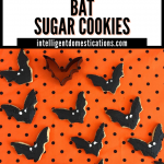 Bat shaped cookies decorated in black icing with white eyes on an orange and black polka dot cloth