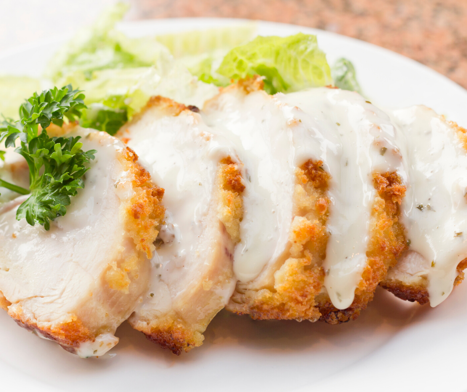 Lightly battered Chicken Cordon Bleu served on a white platter with a creamy sauce poured over