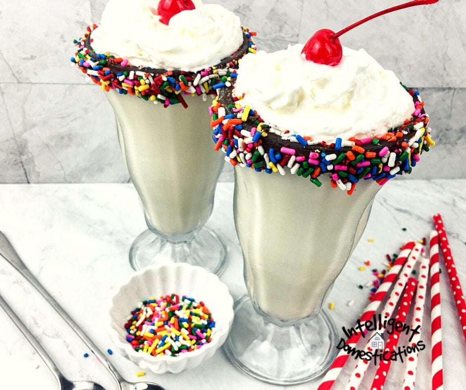 Vanilla milkshakes in tall glasses with chocolate and sprinkles around the rim