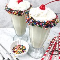 Vanilla milkshakes displayed in a glass with chocolate and sprinkles on the rim
