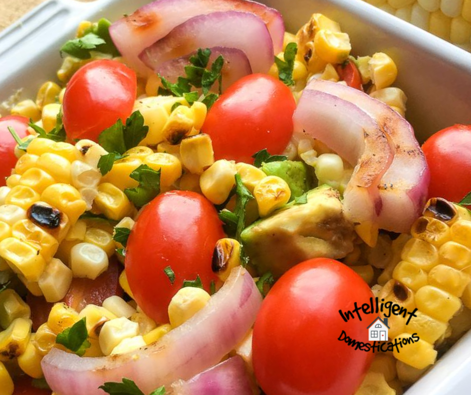 Corn, Tomatoes, Onions and Avocados mixed together in a salad served in a white dish