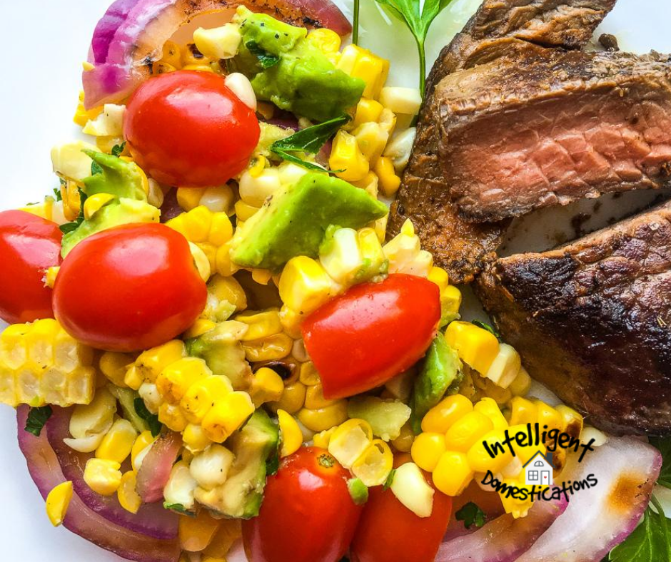 Corn, Tomatoes, Onions and Avocados mixed together in a salad served next to a steak