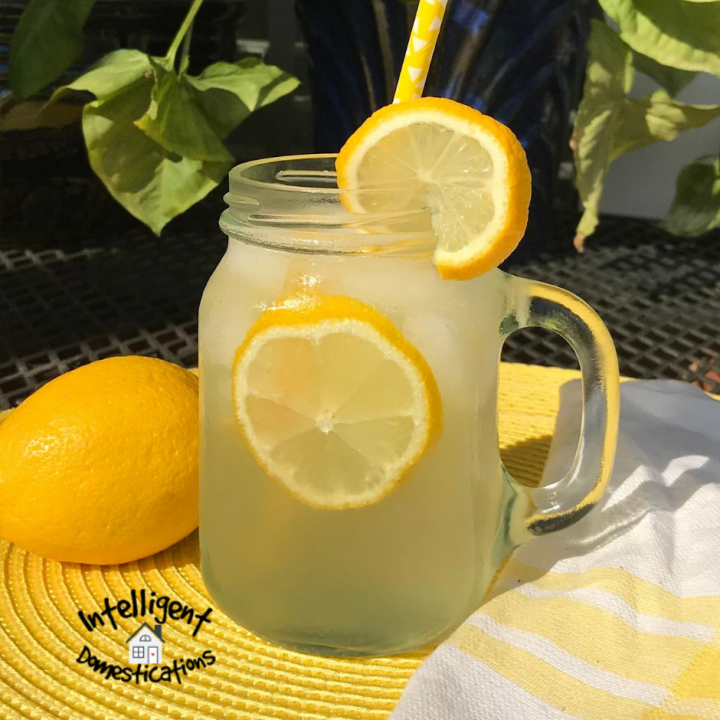 A Mason jar filled with lemonade with lemons floating in it on a yellow place mat in an outdoor dining setting