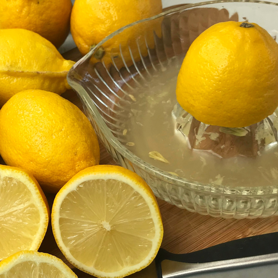 Fresh ripe lemons cut and whole on a cutting board next to a juicer