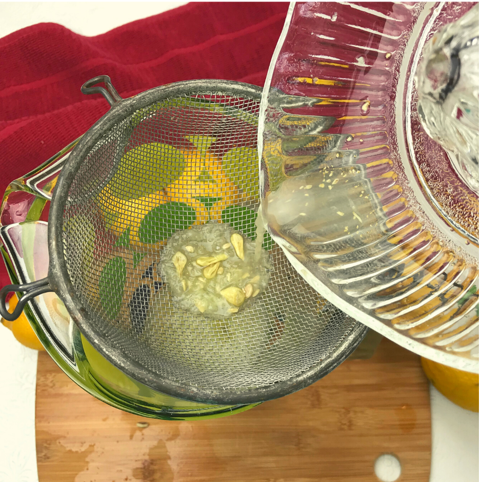 A mesh strainer over a pitcher with lemon juice being poured through it
