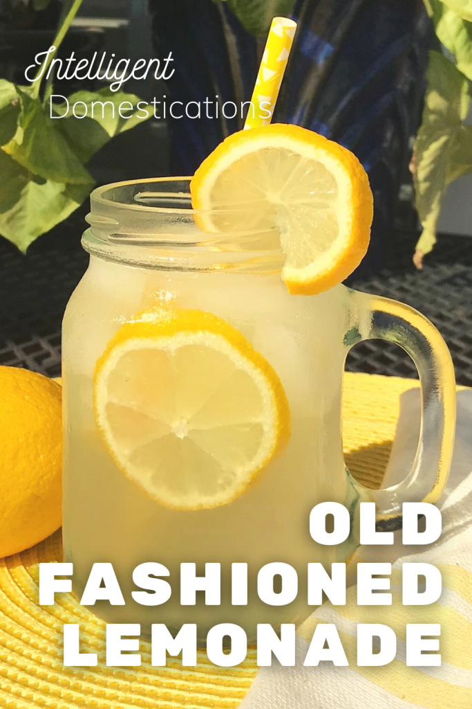 A Mason jar filled with lemonade with lemons floating in it on a yellow place mat in an outdoor dining setting