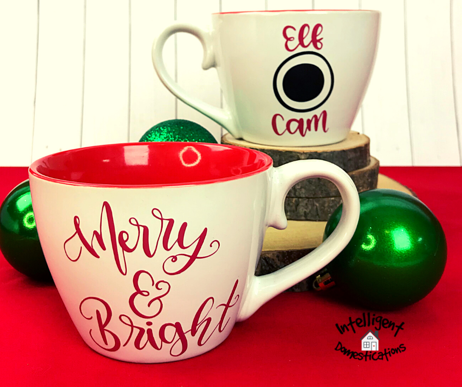 A set of Christmas Elf Cam Mugs displayed on a red cloth with green ornaments