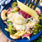 Shrimp pasta and broccoli in a blue bowl with parmesan cheese on top