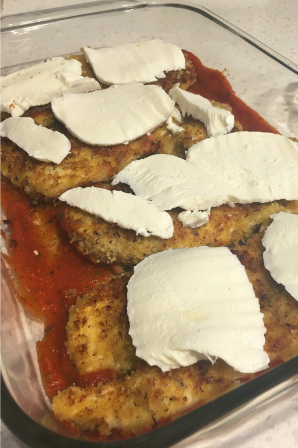Mozzarella cheese slices on top of fried chicken breast in a casserole dish with tomato sauce