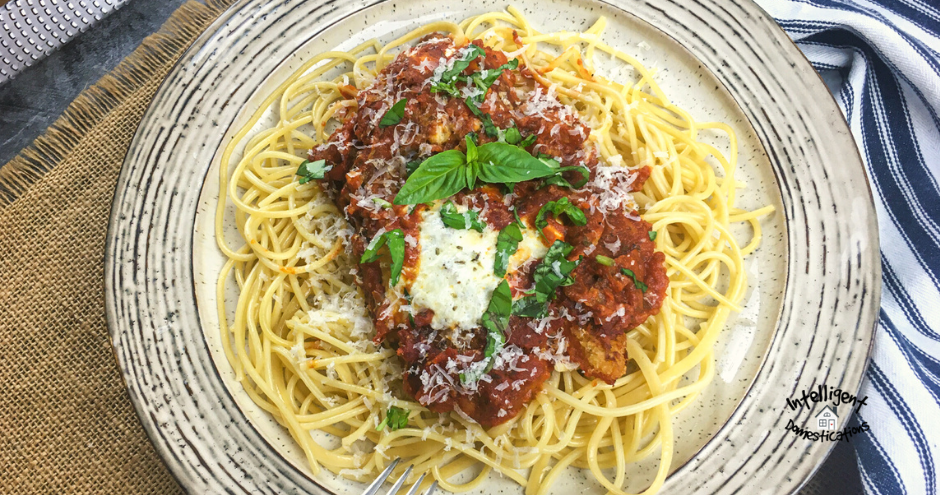 Chicken Parmesan on a bed of spaghetti with chopped Basil on top served on a white dish