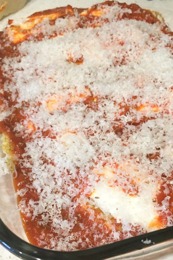 Chicken Parm in a casserole dish with grated parmesan cheese sprinkled on top