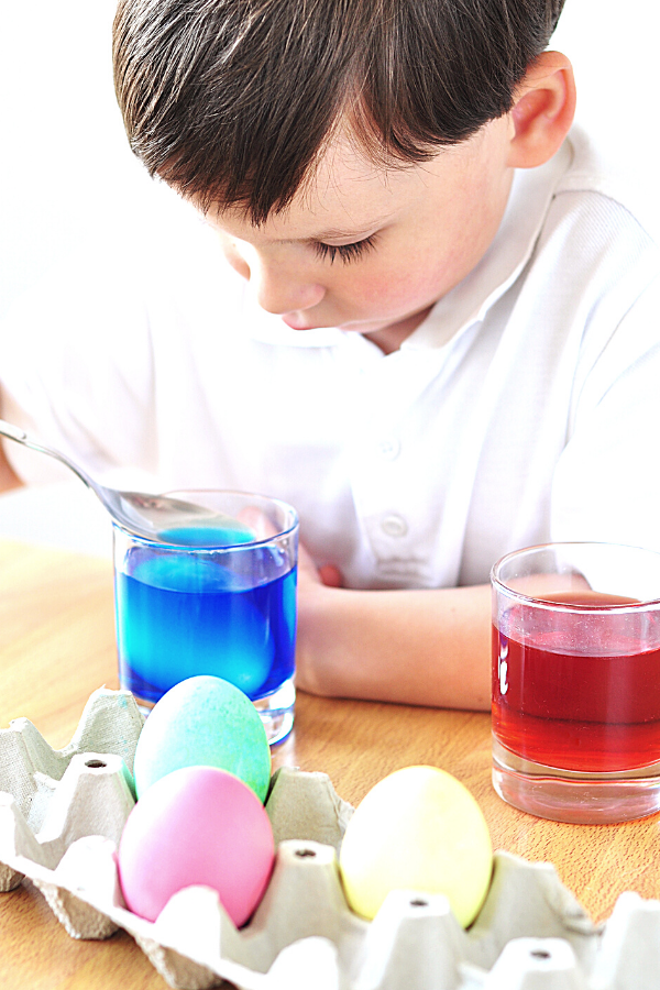 Boy coloring Easter eggs in colored water