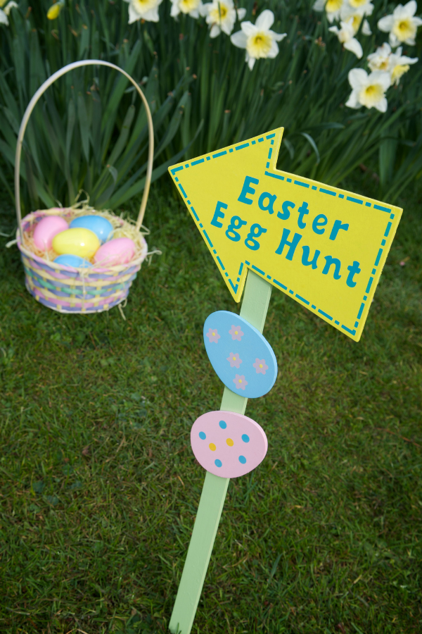 An Easter Egg Hunt sign in the grass next to an Easter basket with plastic eggs