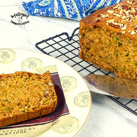 A slice of Pecan Zucchini bread on a plate next the the loaf