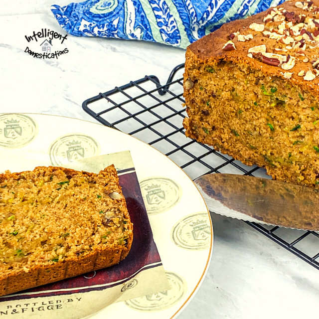 A slice of Pecan Zucchini bread on a plate next the the loaf