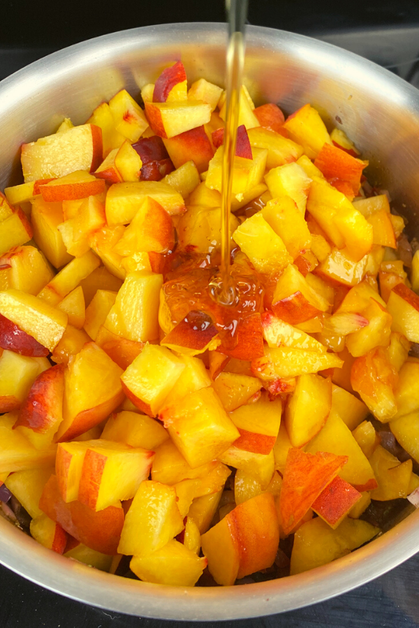pouring honey onto fresh cut peaches in a skillet