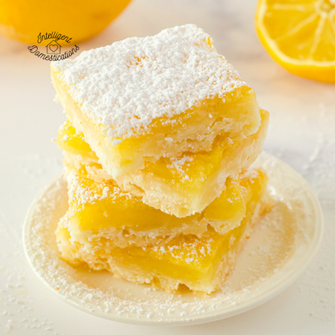 Lemon Bars stacked on a white dish with powdered sugar on top