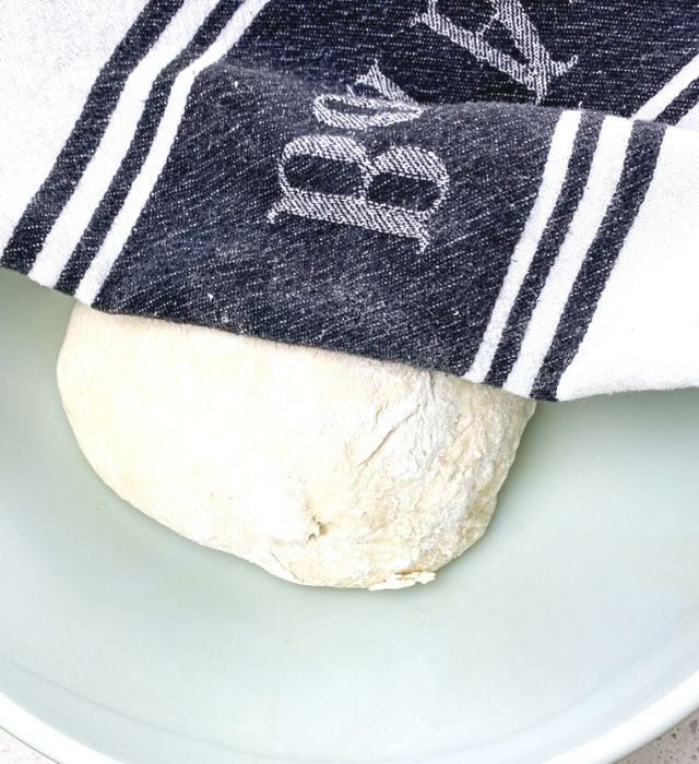 Pretzel dough in a glass bowl covered with a towel so it can rise