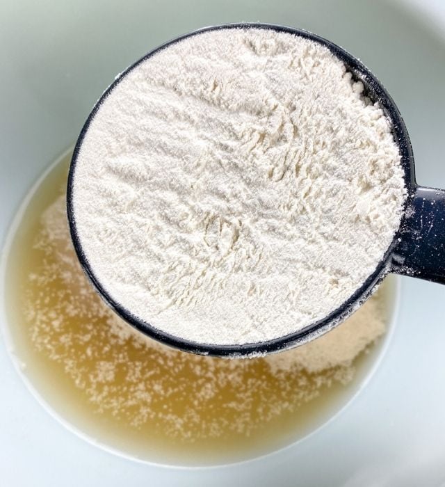 adding flour to bowl with yeast mixture for homemade soft pretzels