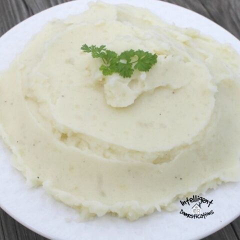 Homemade mashed potatoes in a white bowl with a sprig of parsley on top
