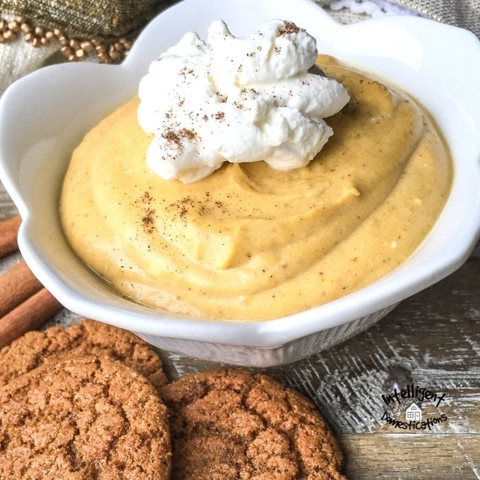 Pumpkin Mousse in a white bowl with whipped cream on top and gingersnap cookies on the side