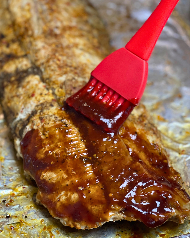 baby back ribs getting BBQ sauce basted onto them