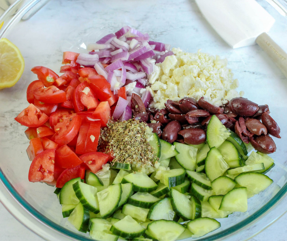 Greek Cucumber Salad Ingredients in a clear glass bowl ready to be tossed