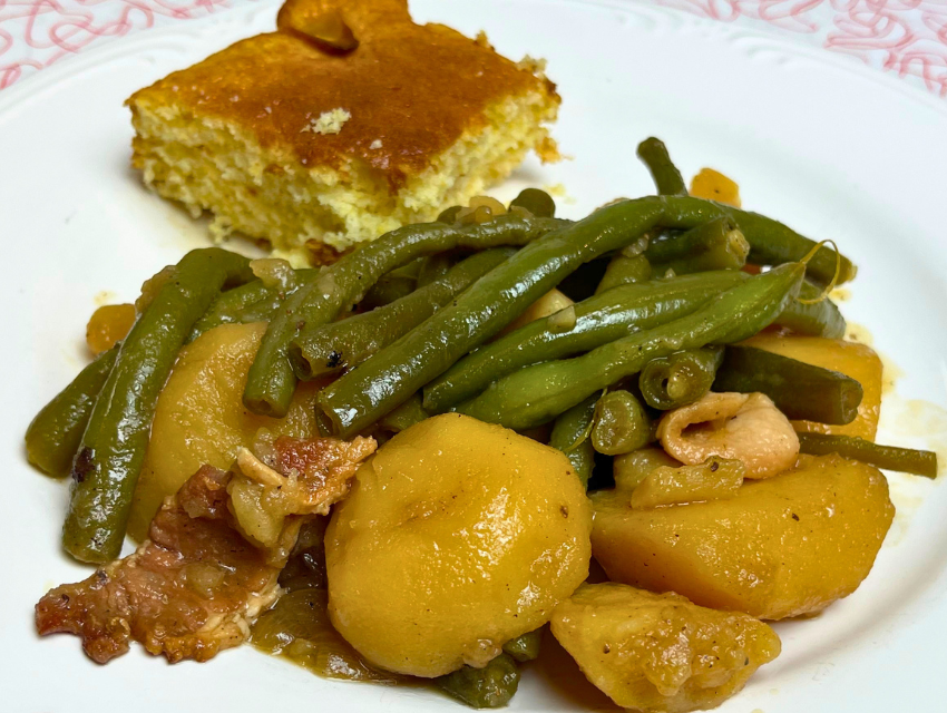 Green beans with potatoes and bacon on a dinner plate with cornbread